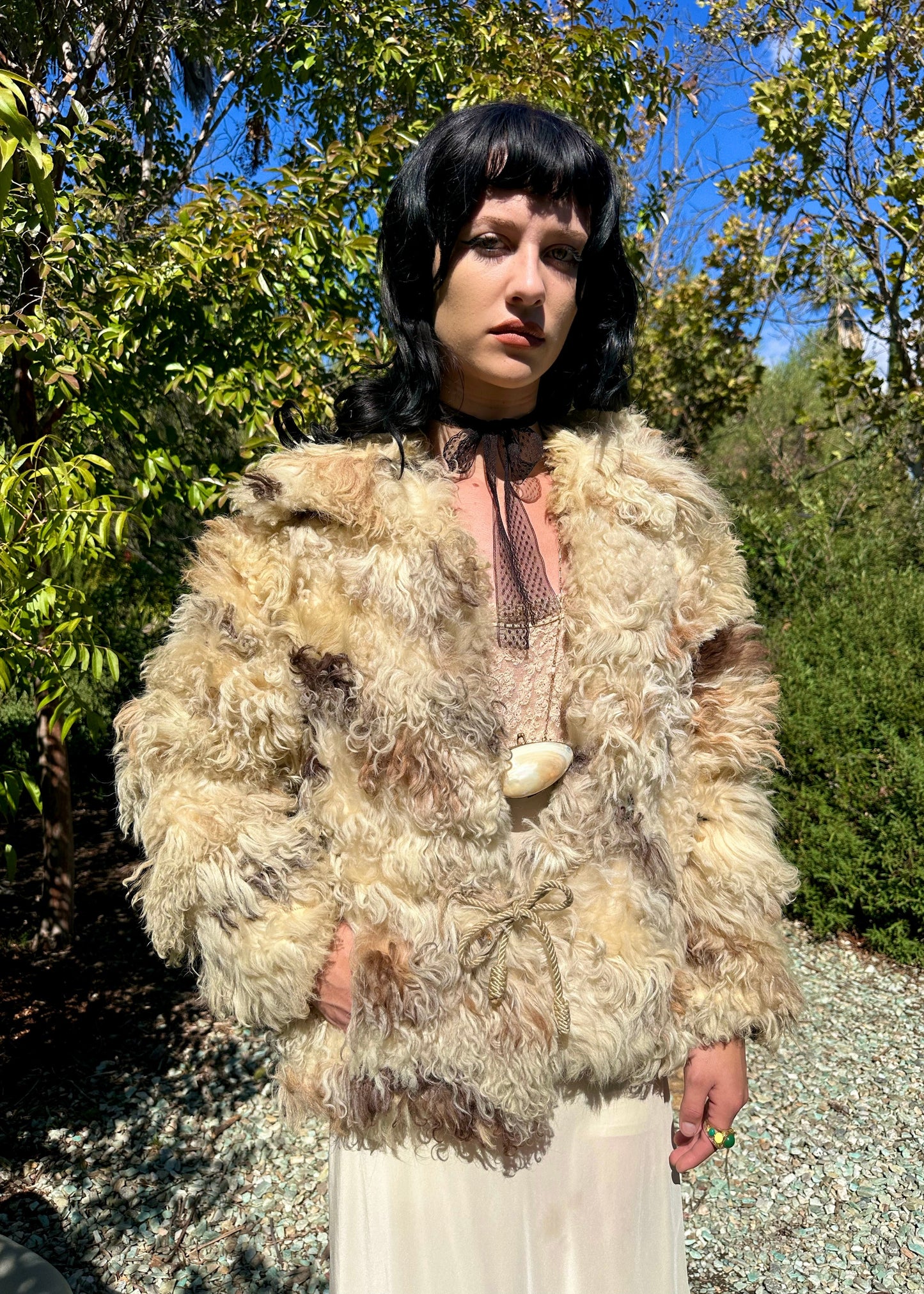 Person wearing a fluffy beige jacket outdoors with trees in the background