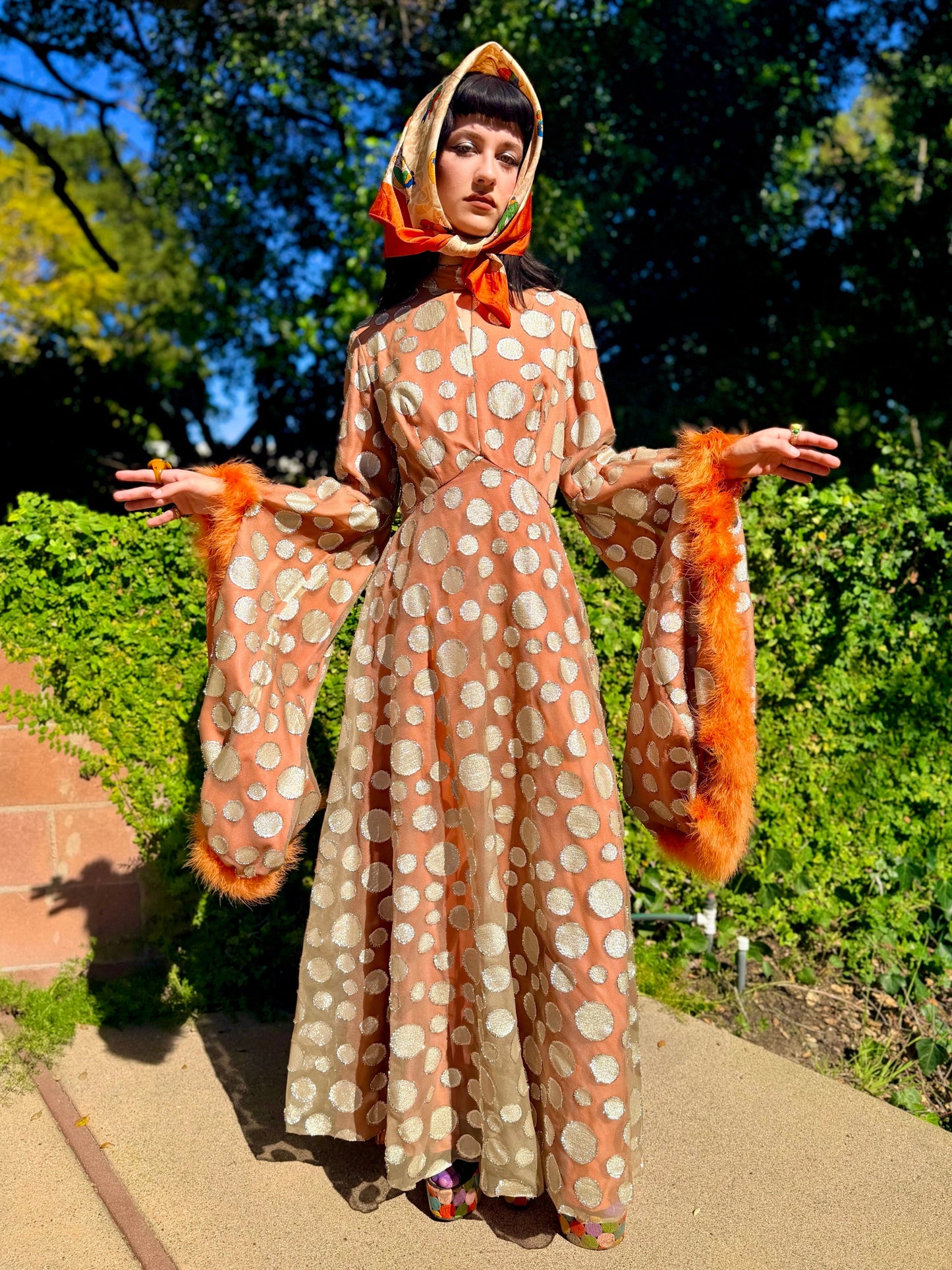 Woman in a vintage 1970s disco glamorous maxi dress with polka dots and orange accents standing outdoors.