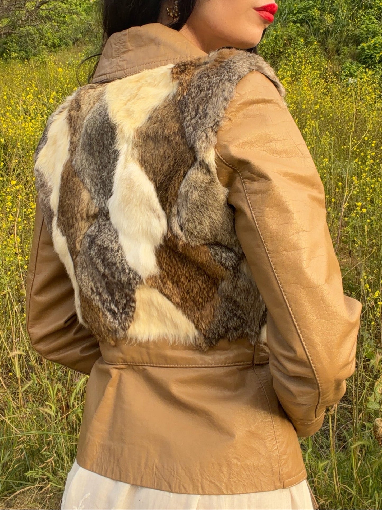 Woman wearing a vintage 1970's leather with fur accents in a natural setting with greenery and yellow flowers.
