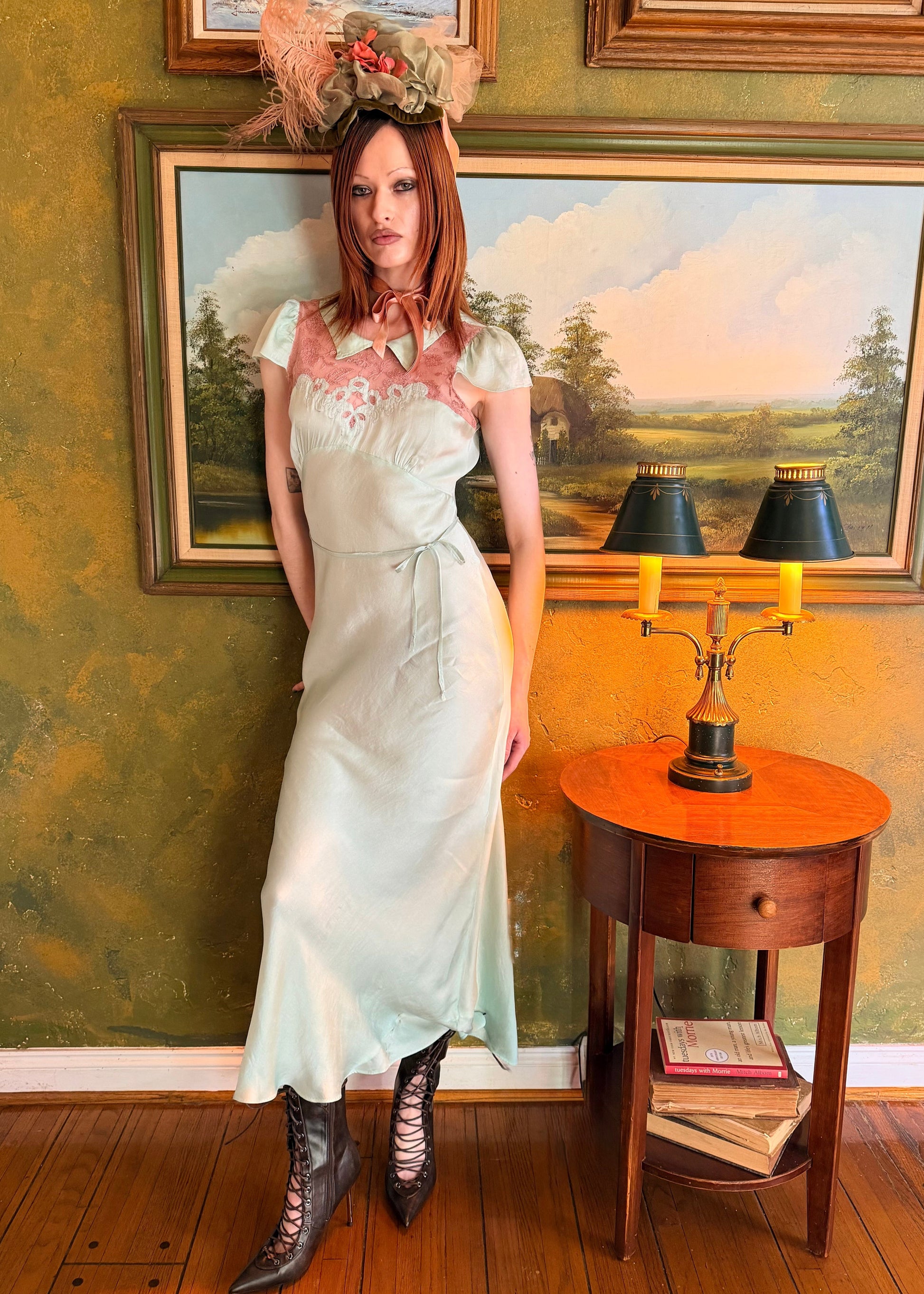 Woman in a vintage dress standing in a room with green walls and framed paintings.