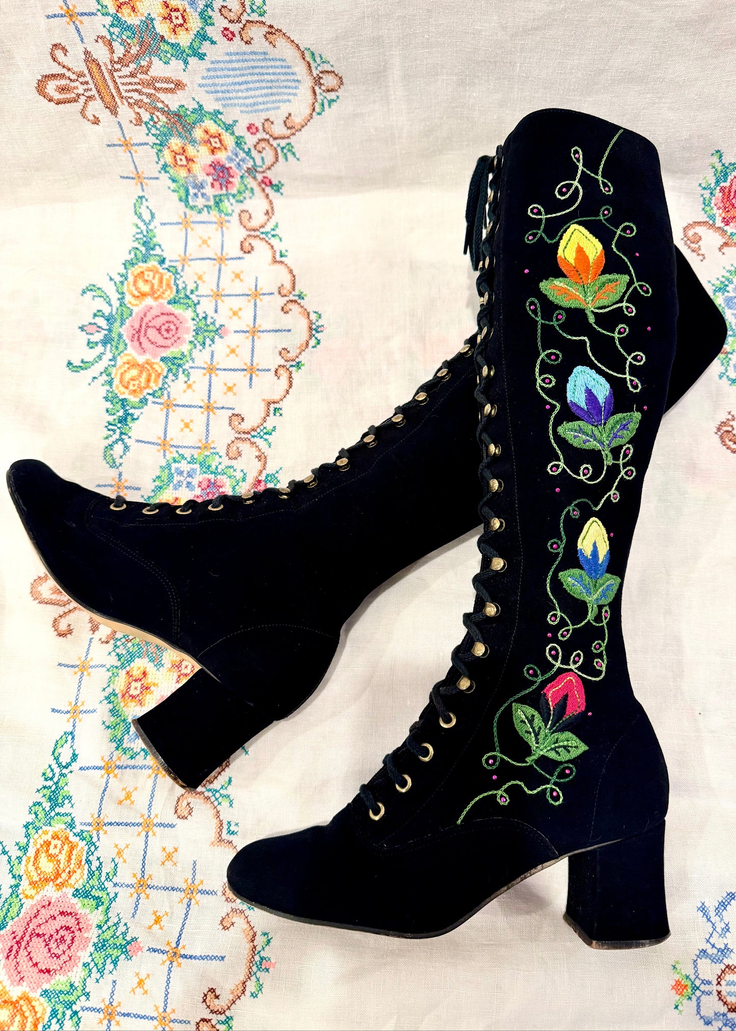 Black knee-high vintage 1960's suede penny lane gogo boots with colorful floral embroidery on a decorative background