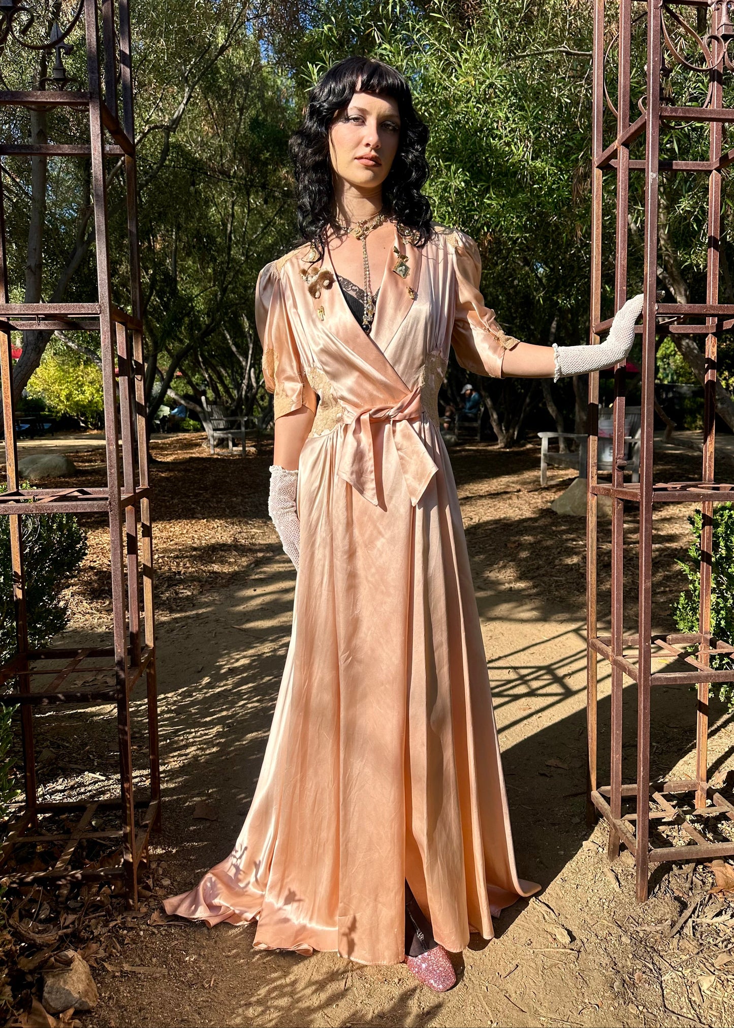 Woman in a vintage-style dress standing between metal arches in a garden setting