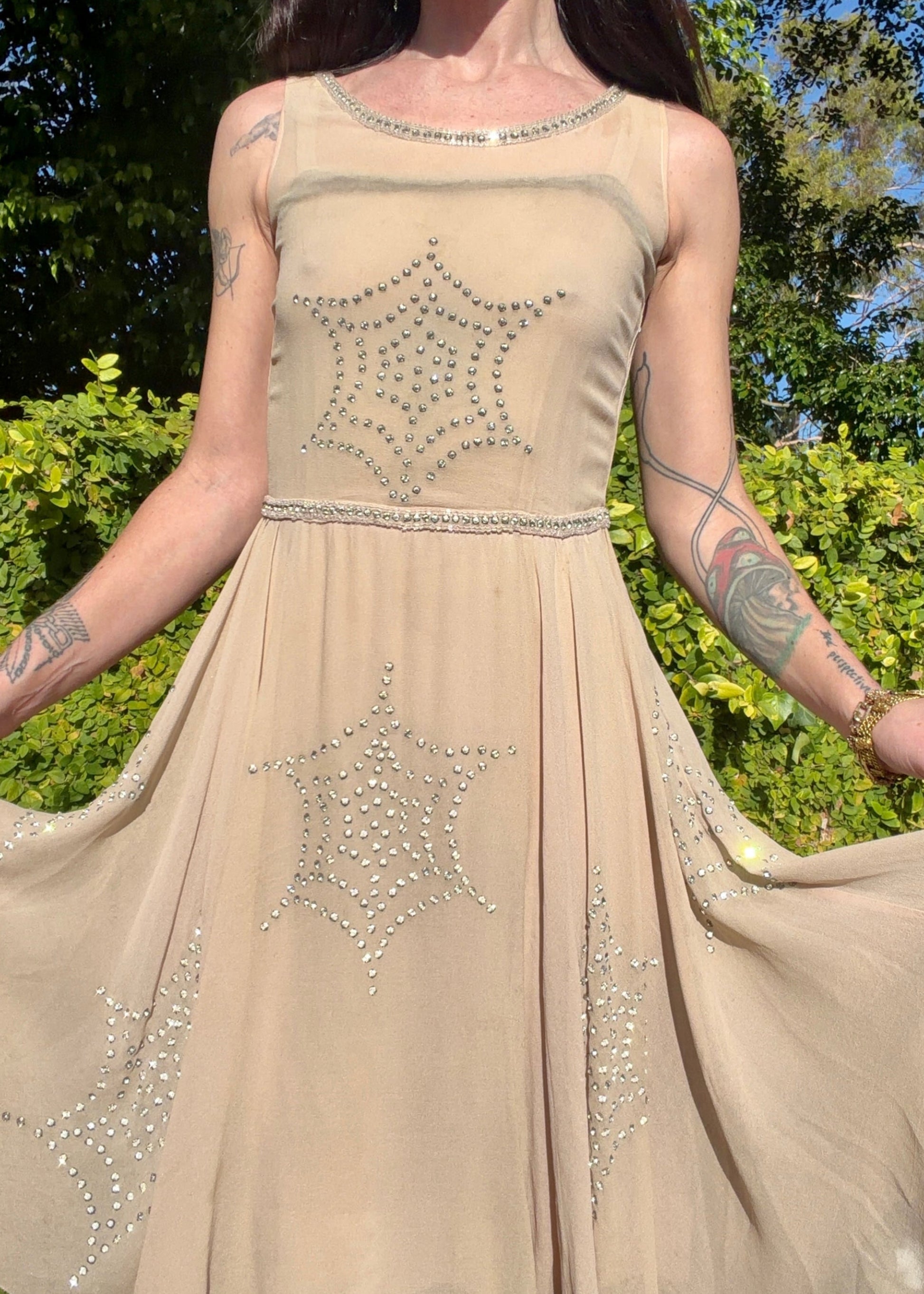 Beige antique 1920's silk chiffon dress with star or spider web design embellishments made from rhinestones worn by a person outdoors.