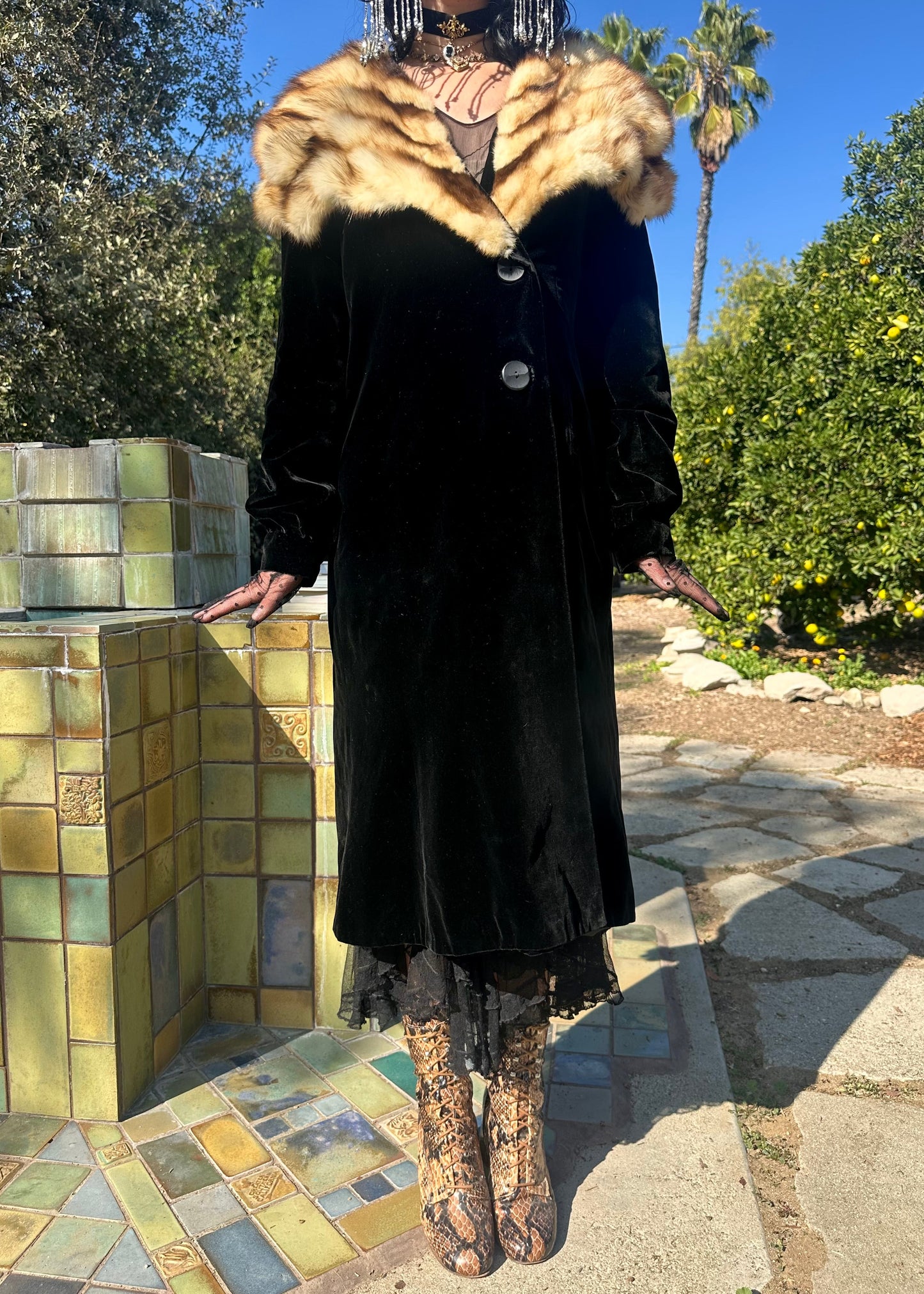 Person wearing an antique 1930s black coat with a fox fur collar standing outdoors.