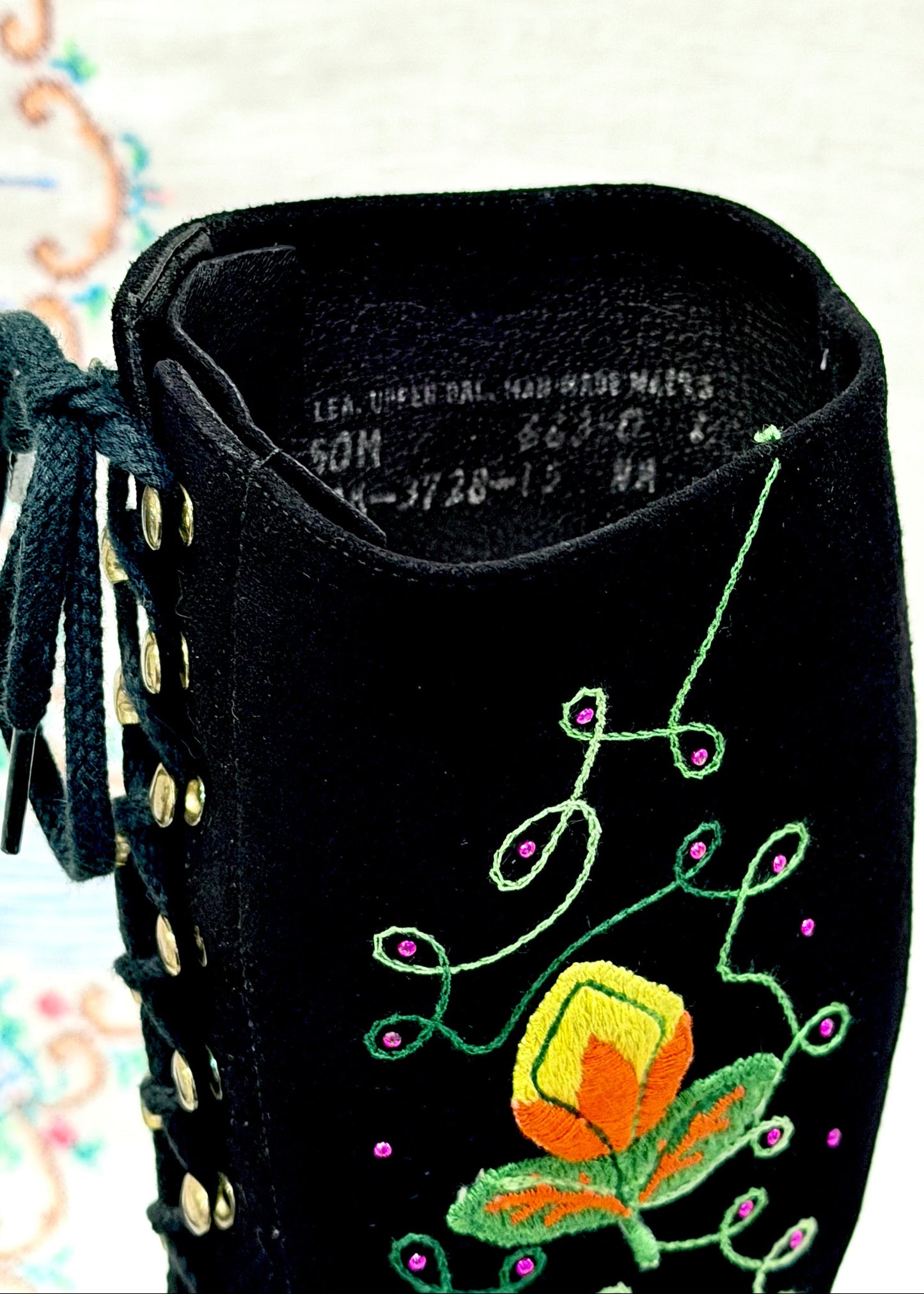 Black knee-high vintage 1960's suede penny lane gogo boots with colorful floral embroidery on a decorative background