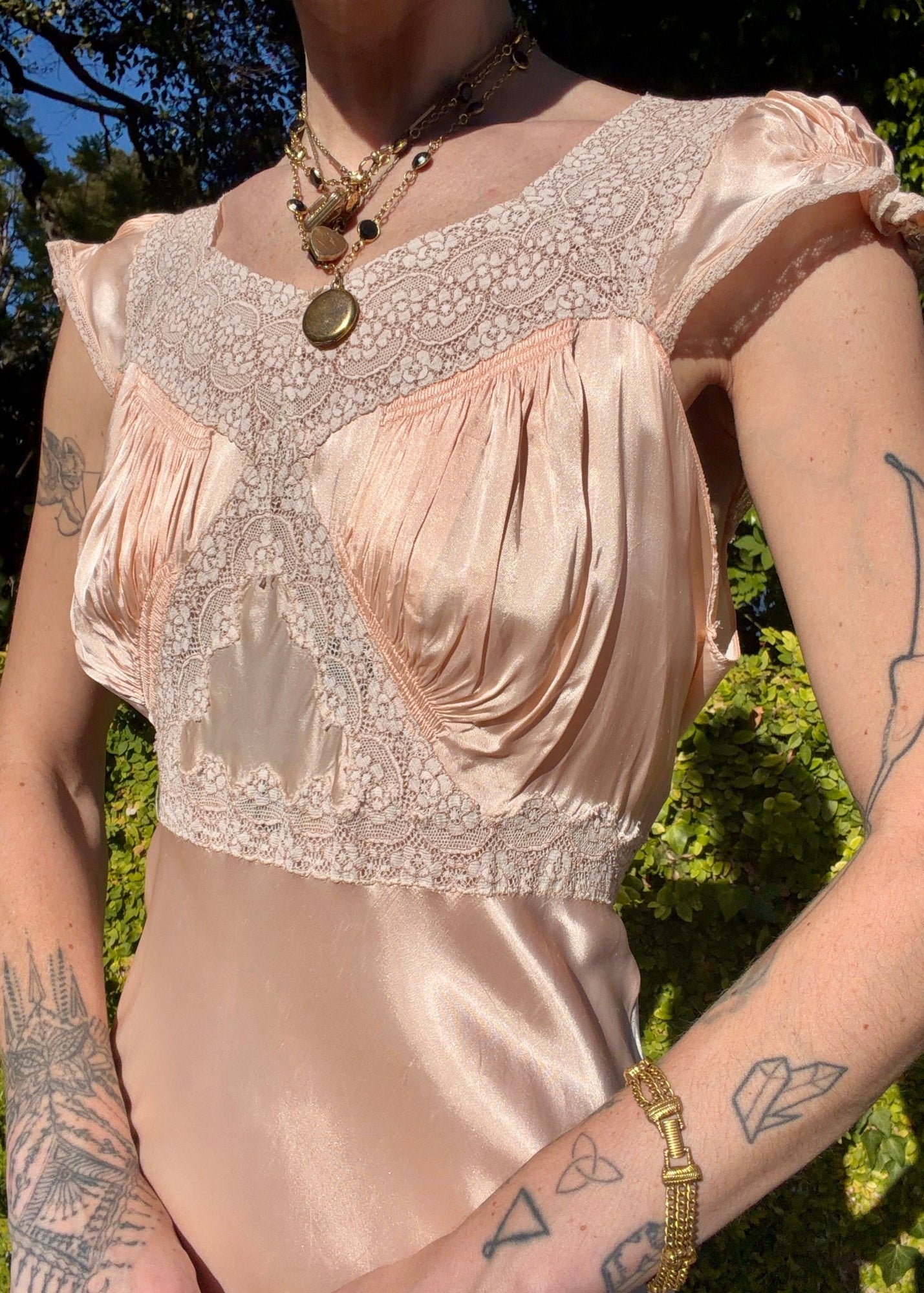 Woman wearing a long bias cut, elegant antique 1930's silk slip dress in a light pink color in an outdoor setting.
