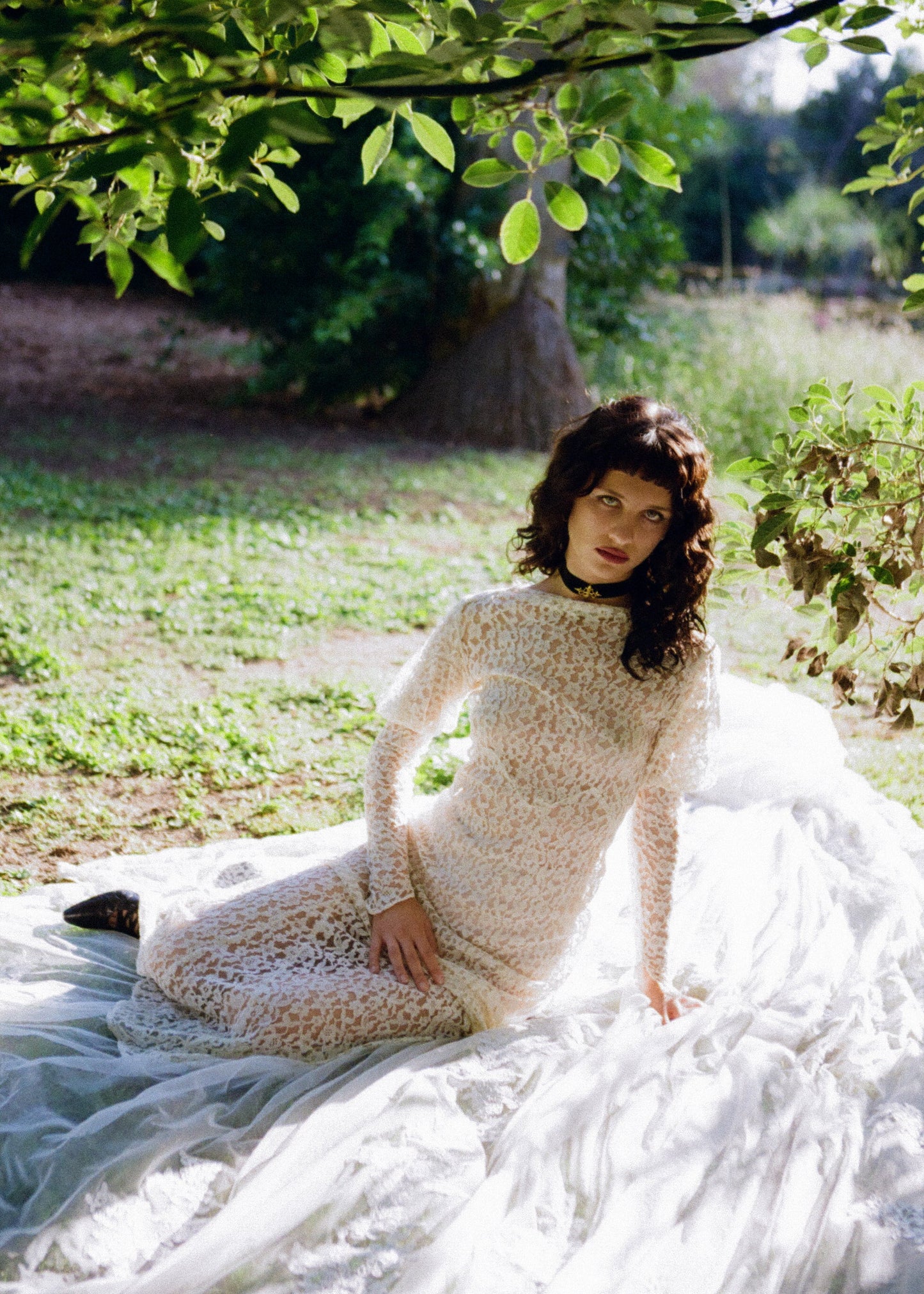 Woman wearing antique lace wedding dress standing outdoors with greenery in the background