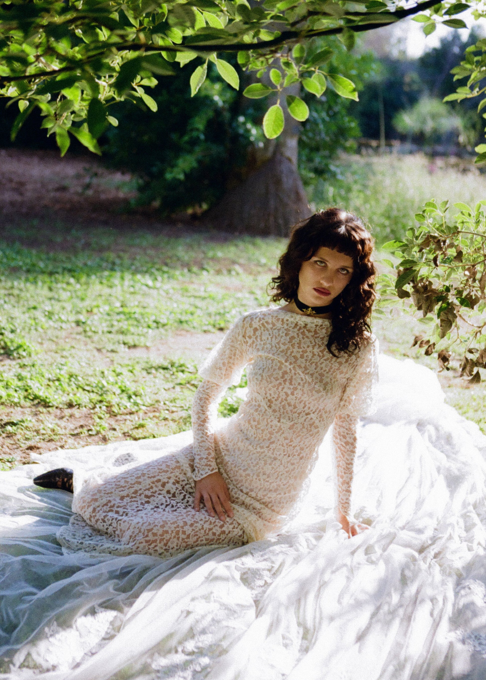 Woman wearing antique lace wedding dress standing outdoors with greenery in the background