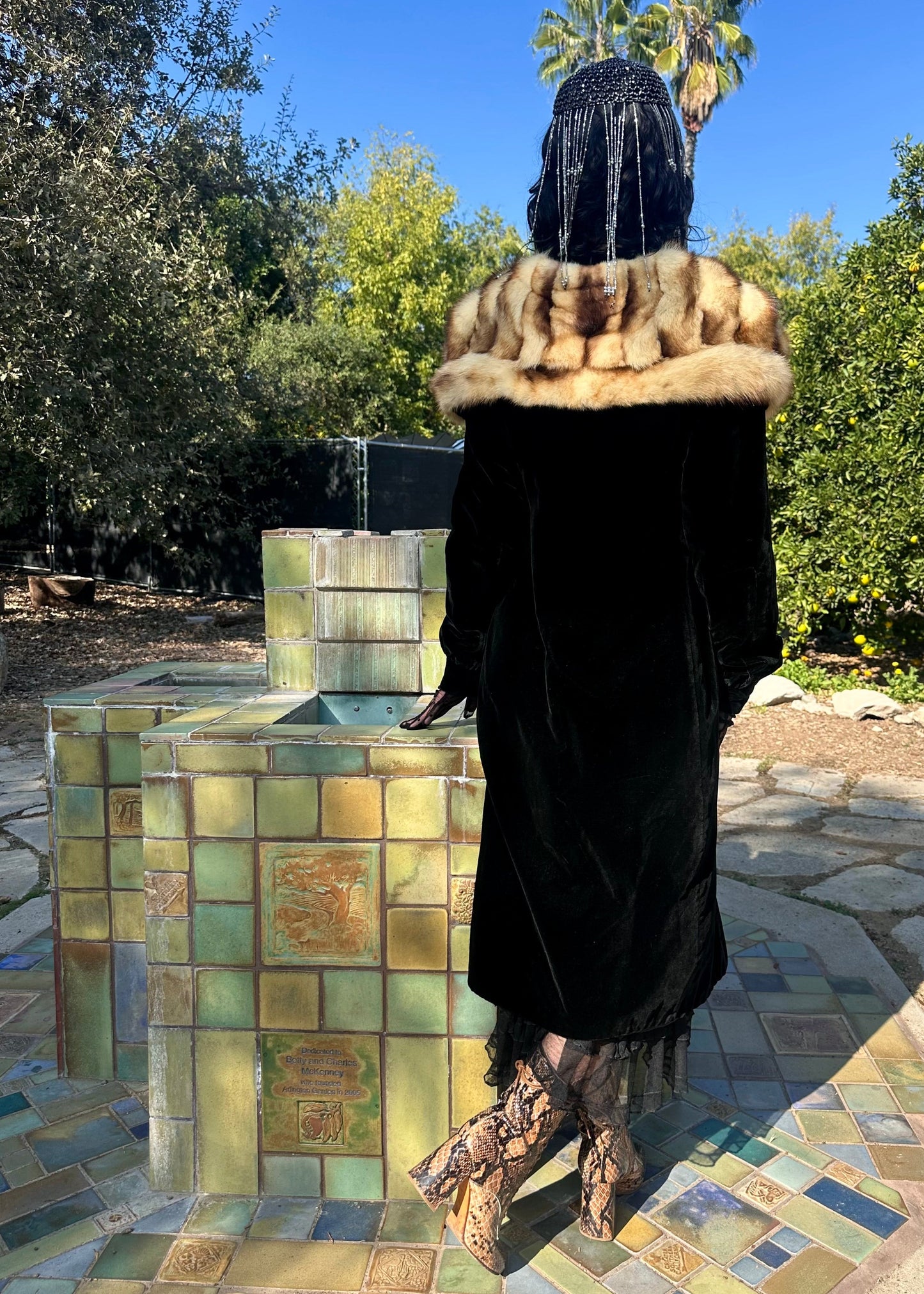 Person in an antique 1930's silk velvet coat with fur stole standing in front of a mosaic fountain.