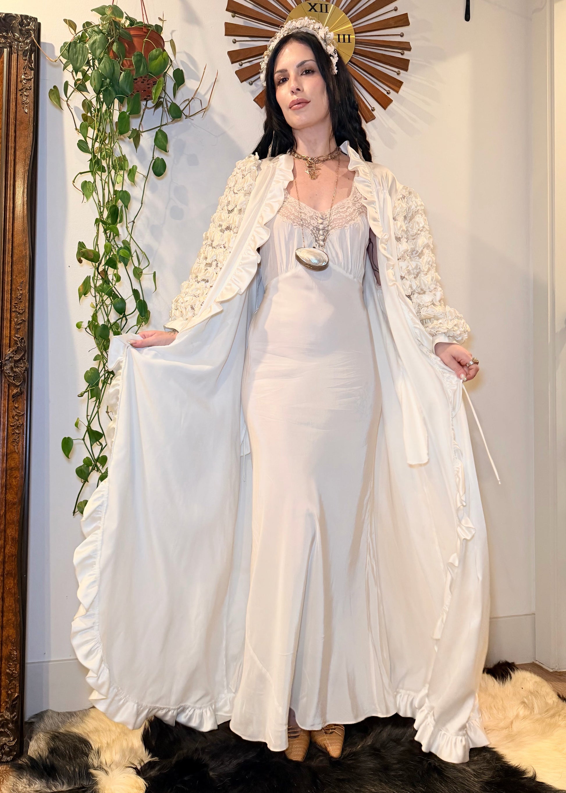 Woman in a white 1930s bias cut dress standing in a room with decorative elements.