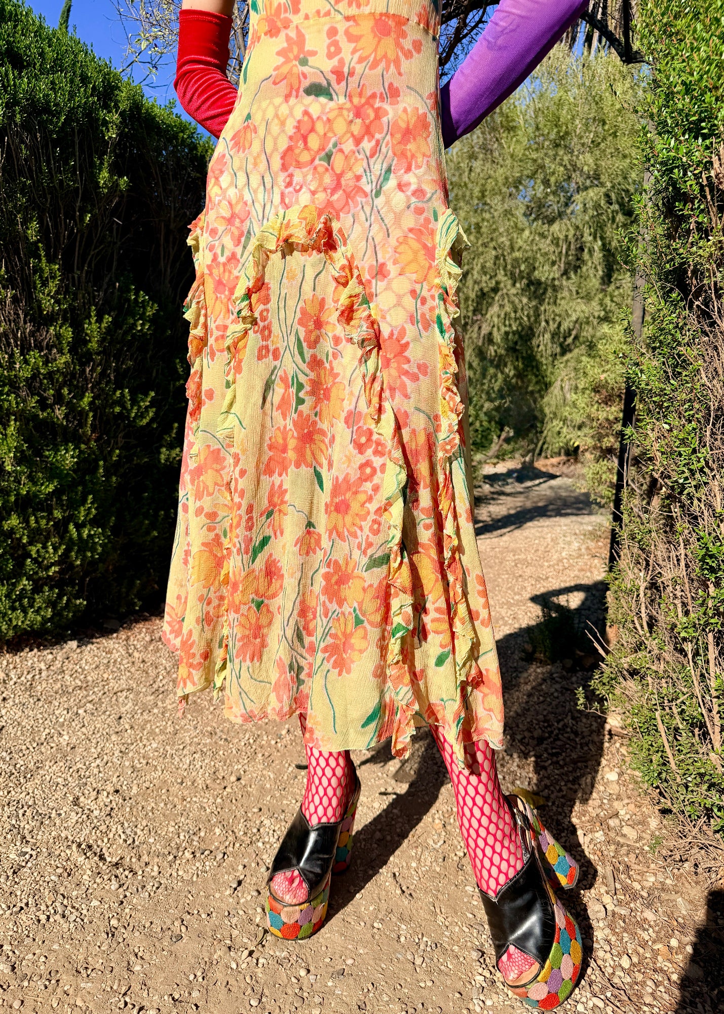 Woman in a colorful antique 1920's silk dress and hat standing outdoors with greenery and blue sky in the background