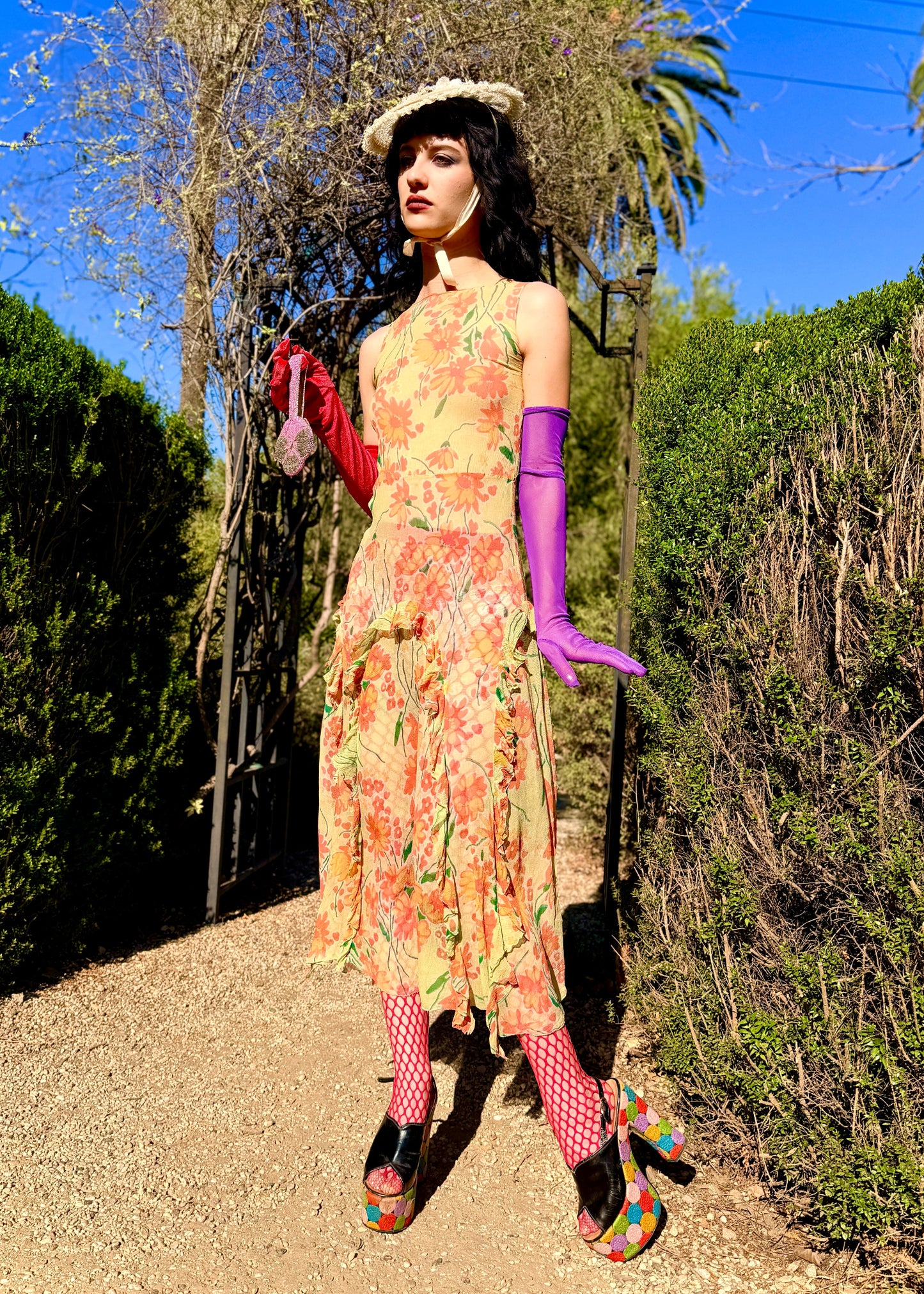 Woman in a colorful antique 1920's silk dress and hat standing outdoors with greenery and blue sky in the background