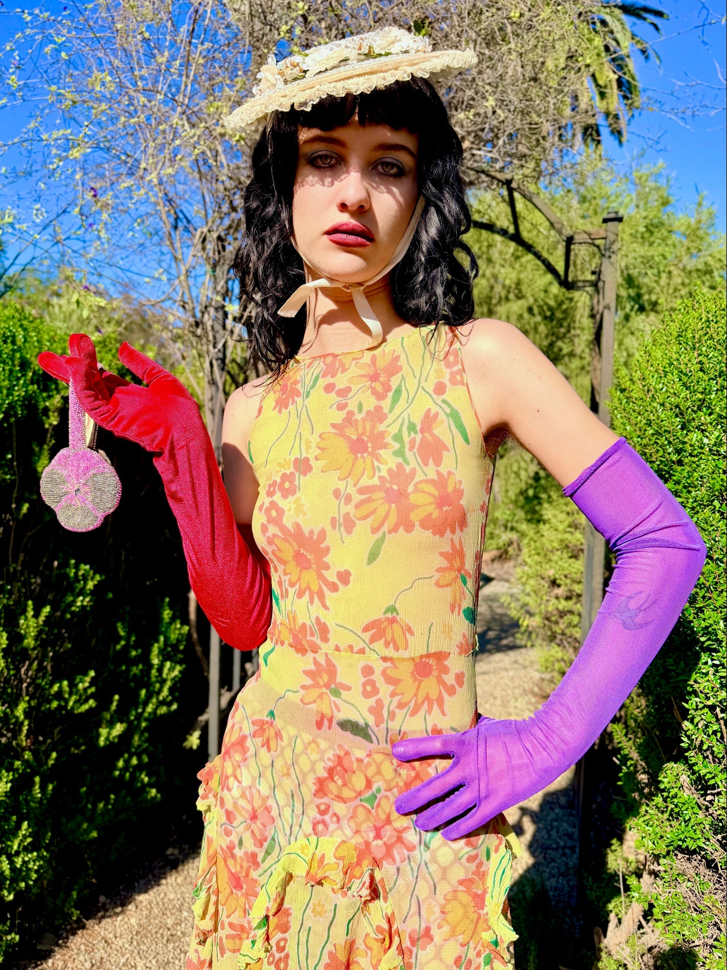 Woman in a colorful antique 1920's silk dress and hat standing outdoors with greenery and blue sky in the background