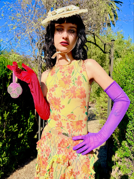 Woman in a colorful antique 1920's silk dress and hat standing outdoors with greenery and blue sky in the background