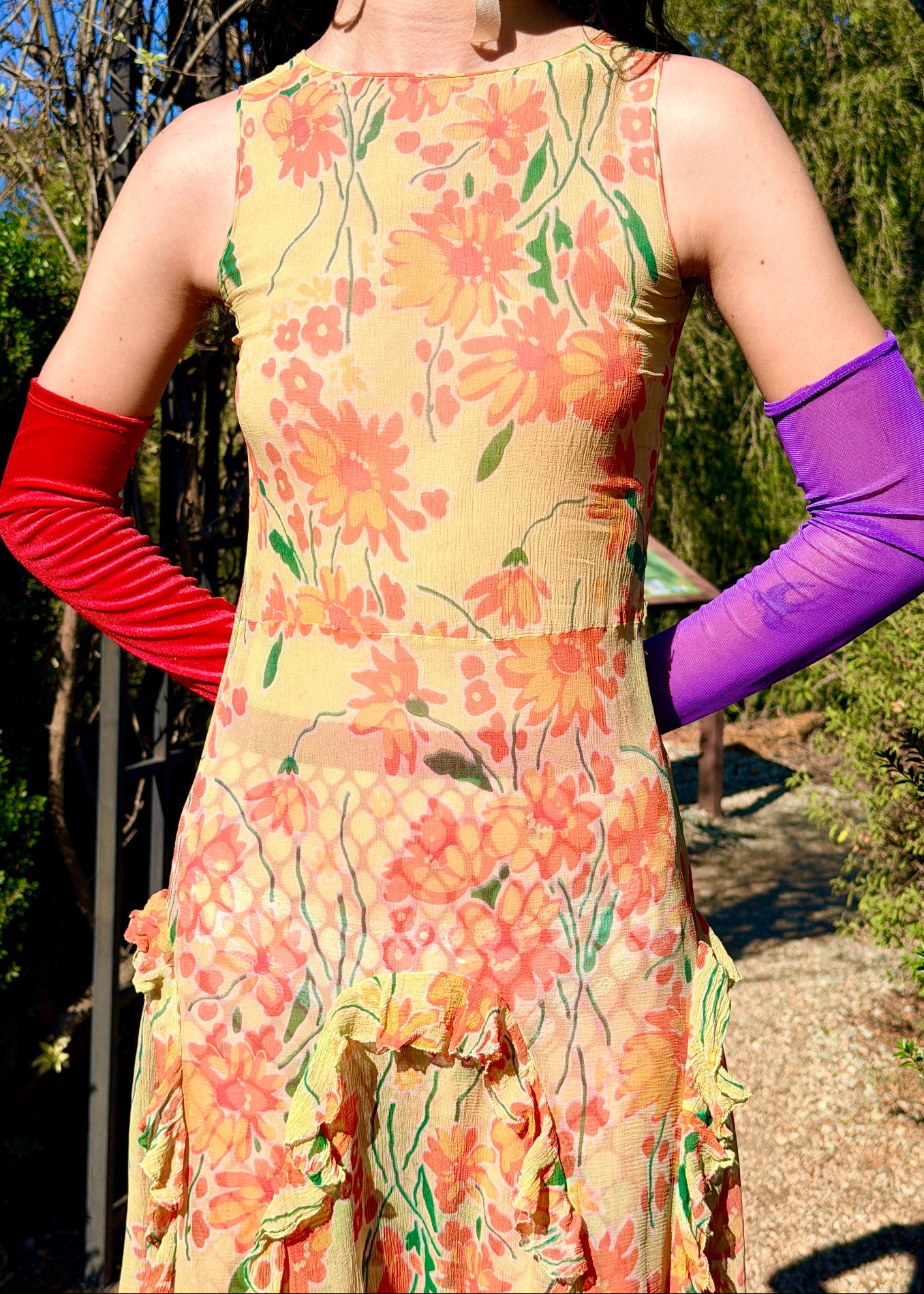 Woman in a colorful antique 1920's silk dress and hat standing outdoors with greenery and blue sky in the background