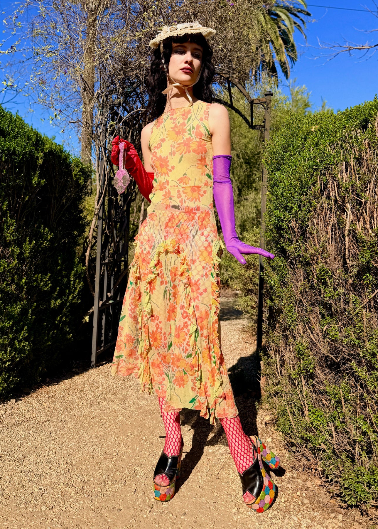 Woman in a colorful antique 1920's silk dress and hat standing outdoors with greenery and blue sky in the background