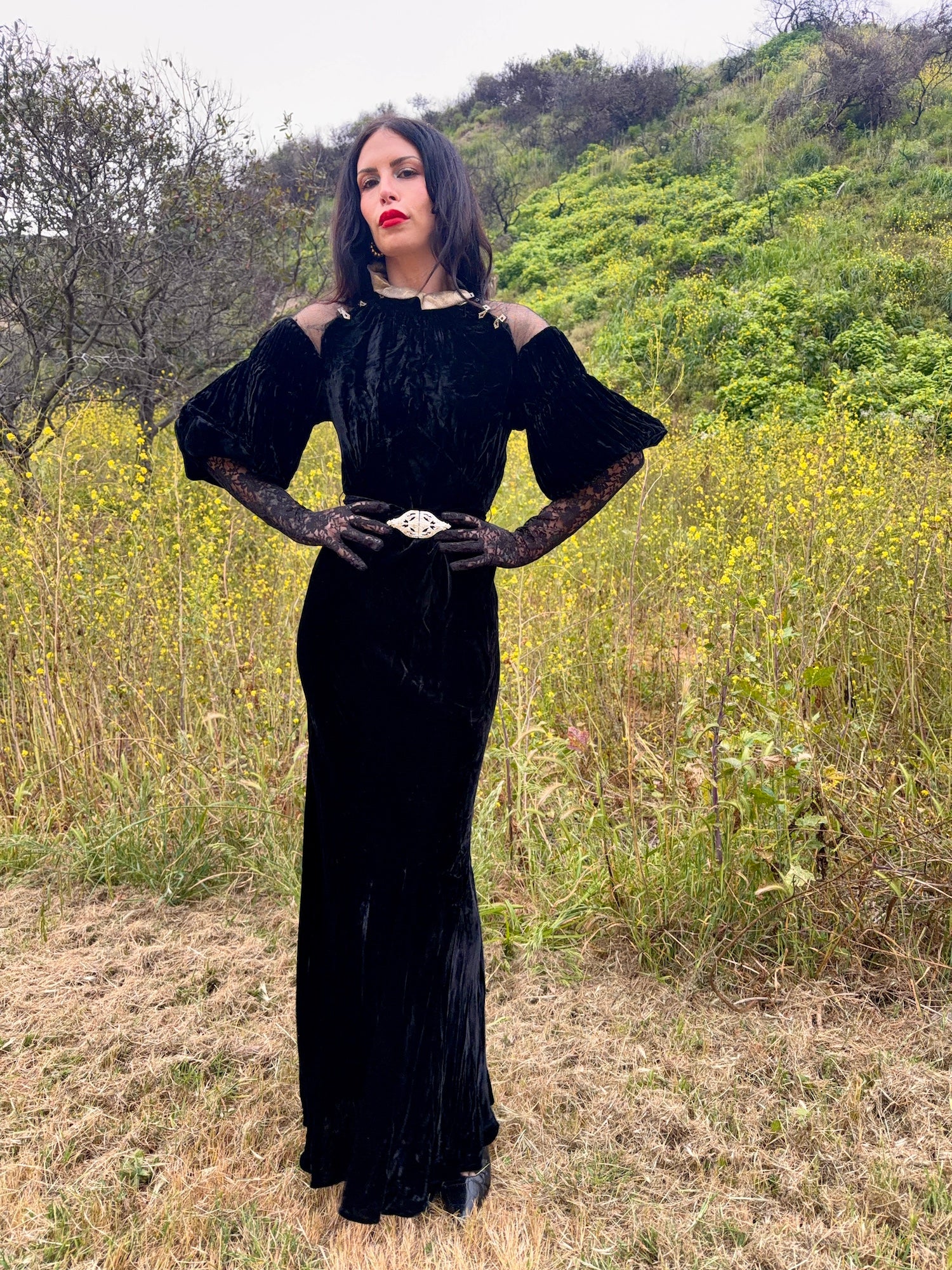 Woman wears antique 1930's black silk velvet Art Deco evening gown in field