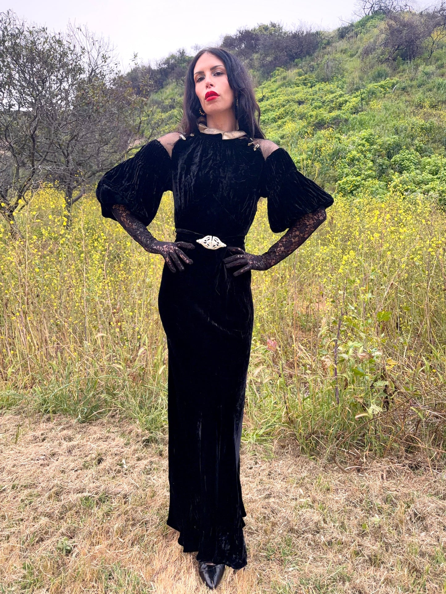 Woman wears antique 1930's black silk velvet Art Deco evening gown in field