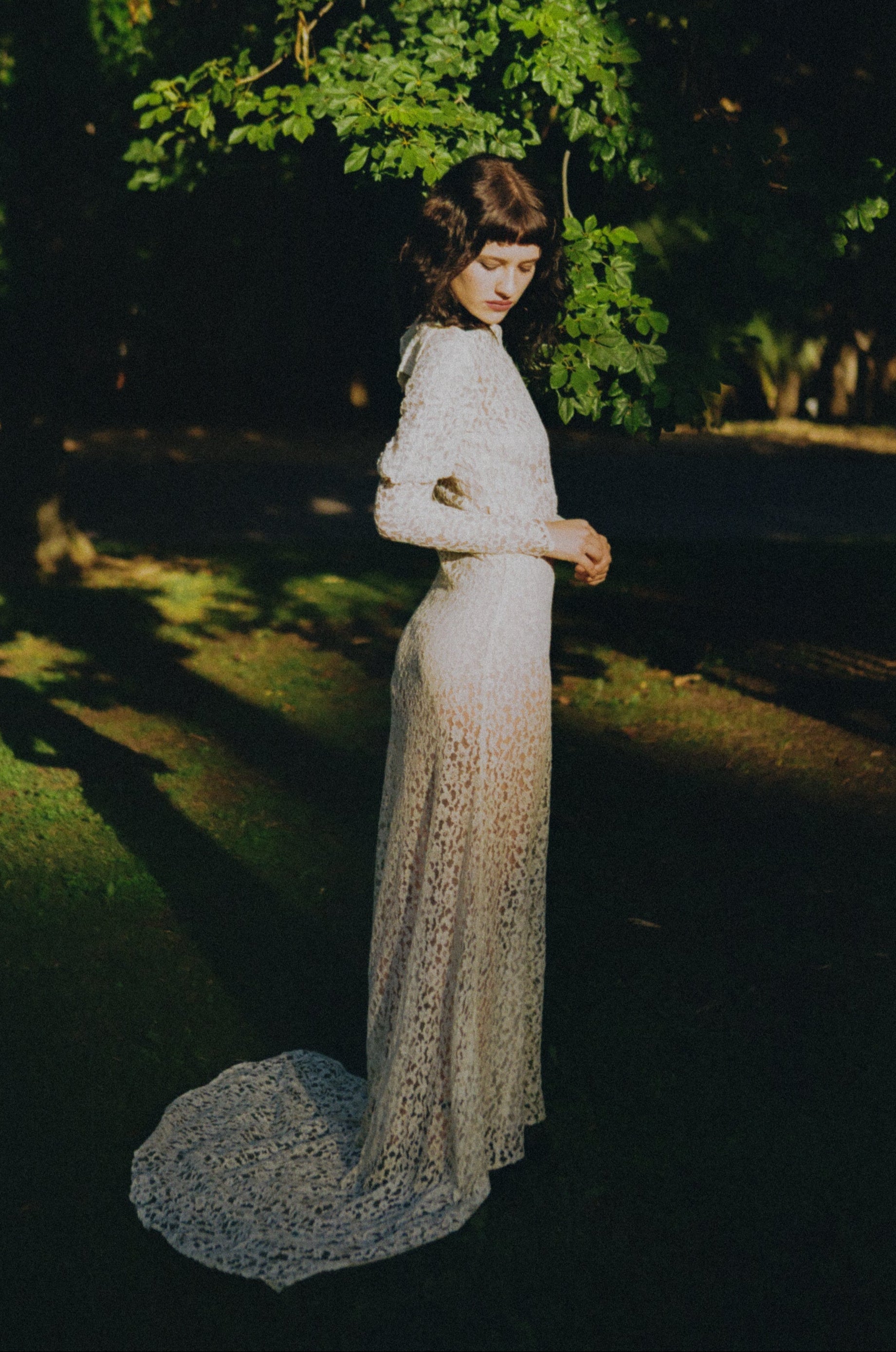 Woman in a white lace dress standing in a dark forest with trees in the background