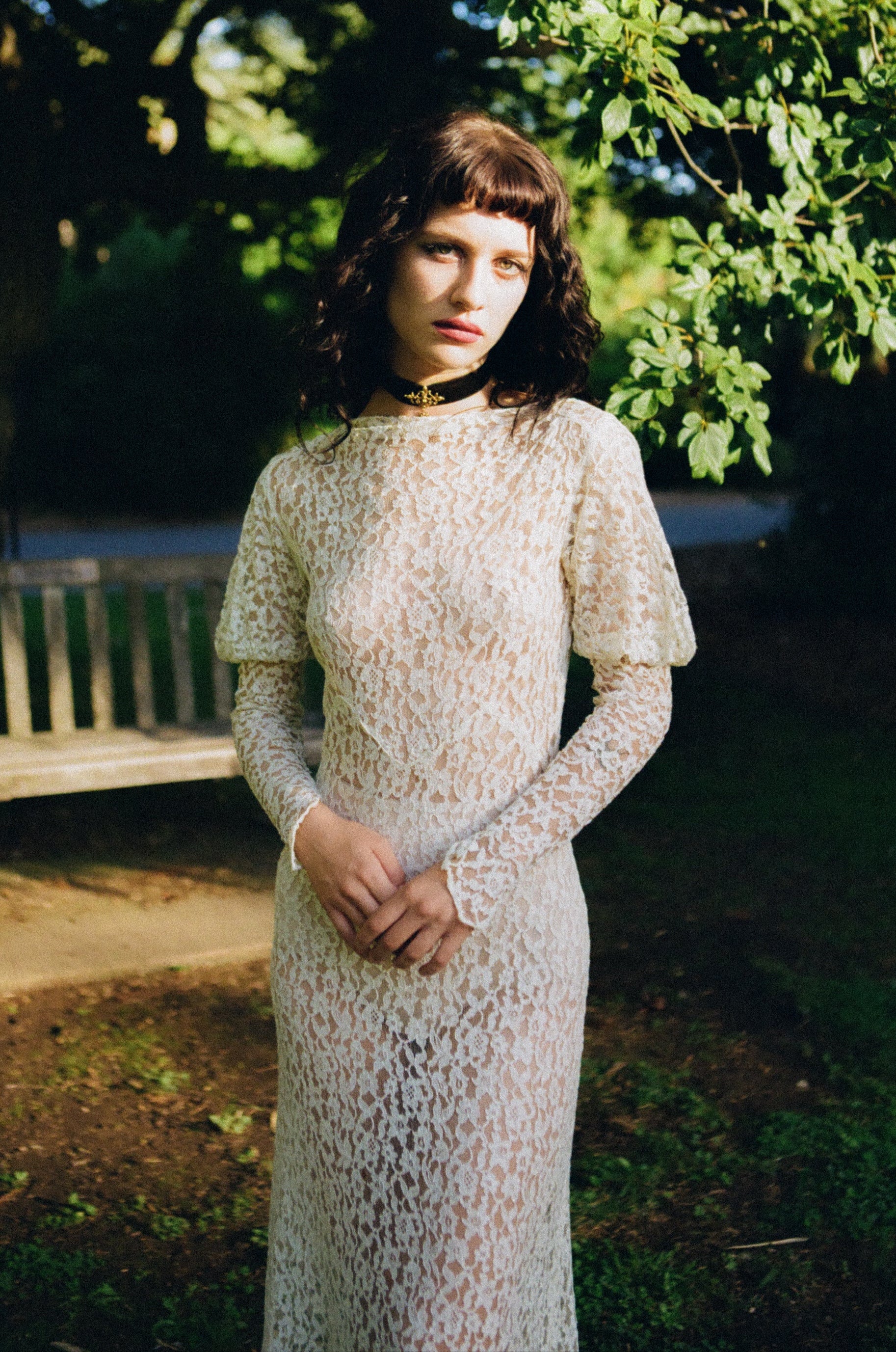 Woman wearing a lace dress standing outdoors with greenery in the background