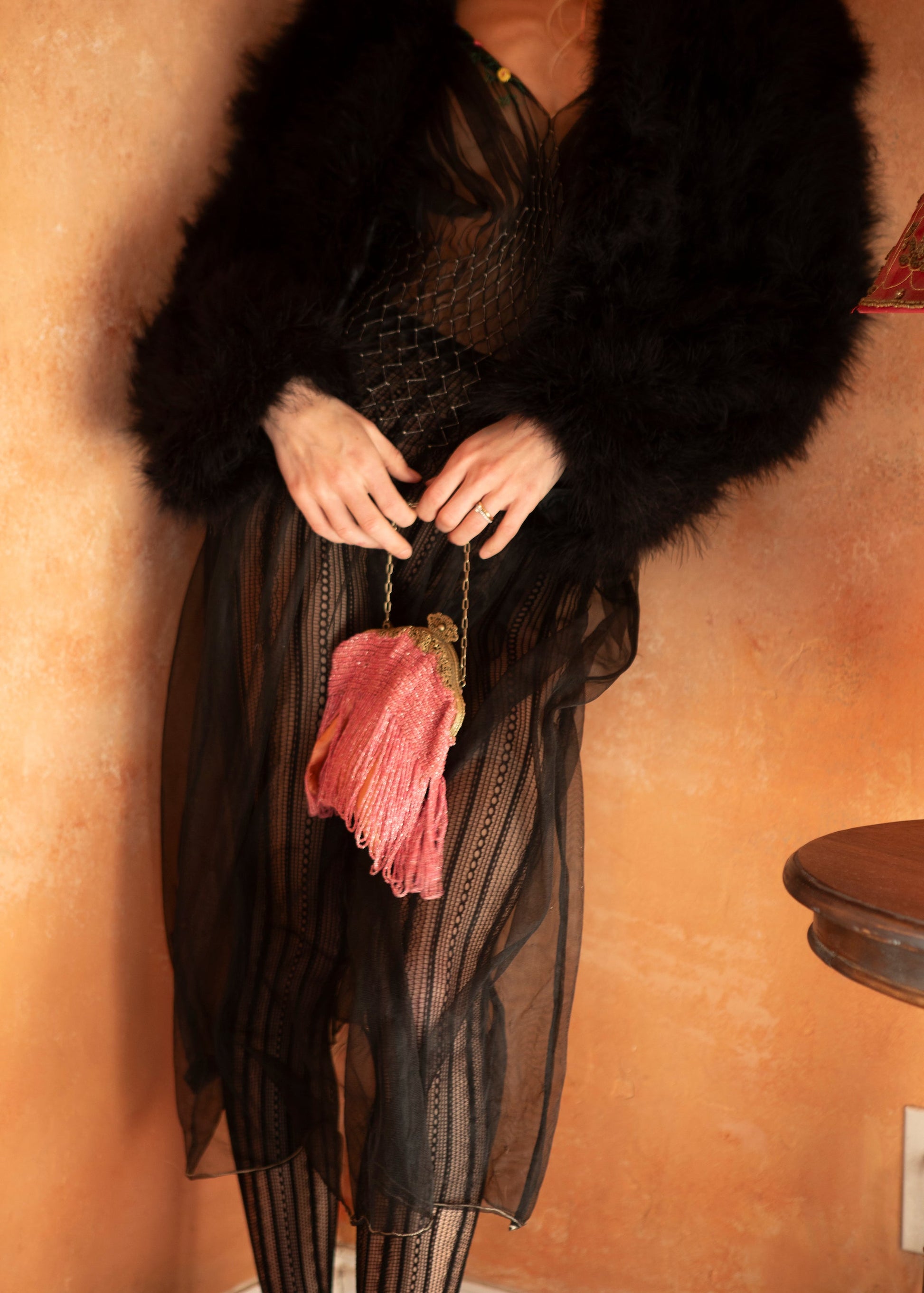 Woman wearing a black marabou feather coat sitting on a chair with a red curtain in the background