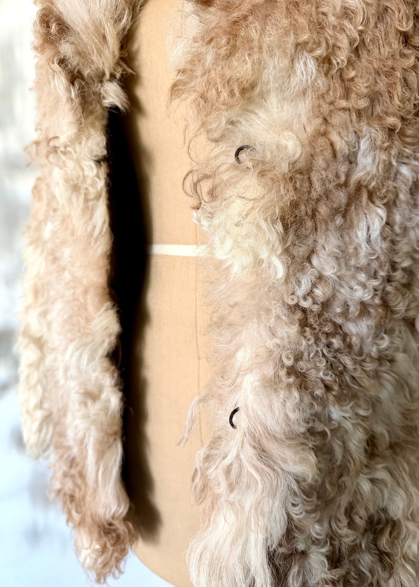 Close-up of a person wearing a beige sherpa jacket with a blurred background