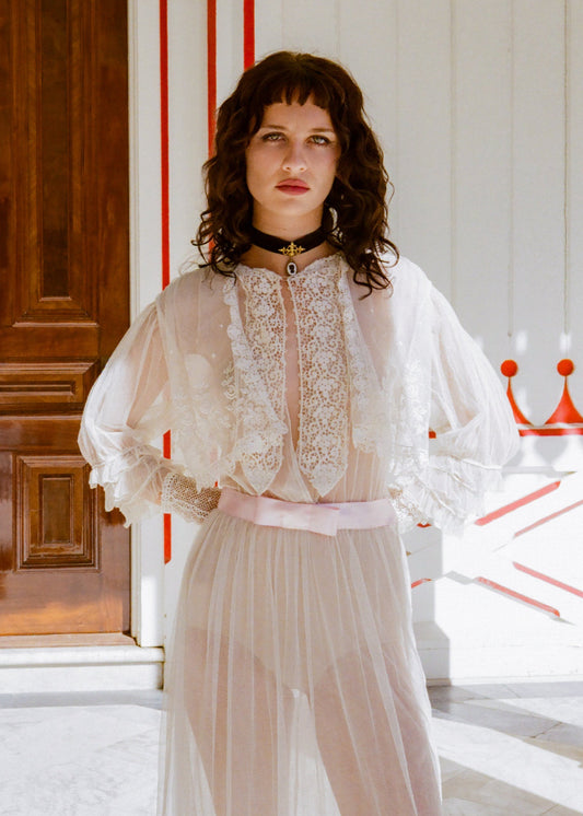 Woman wearing a white lace top and light-colored skirt in a room with wooden door and red accents.