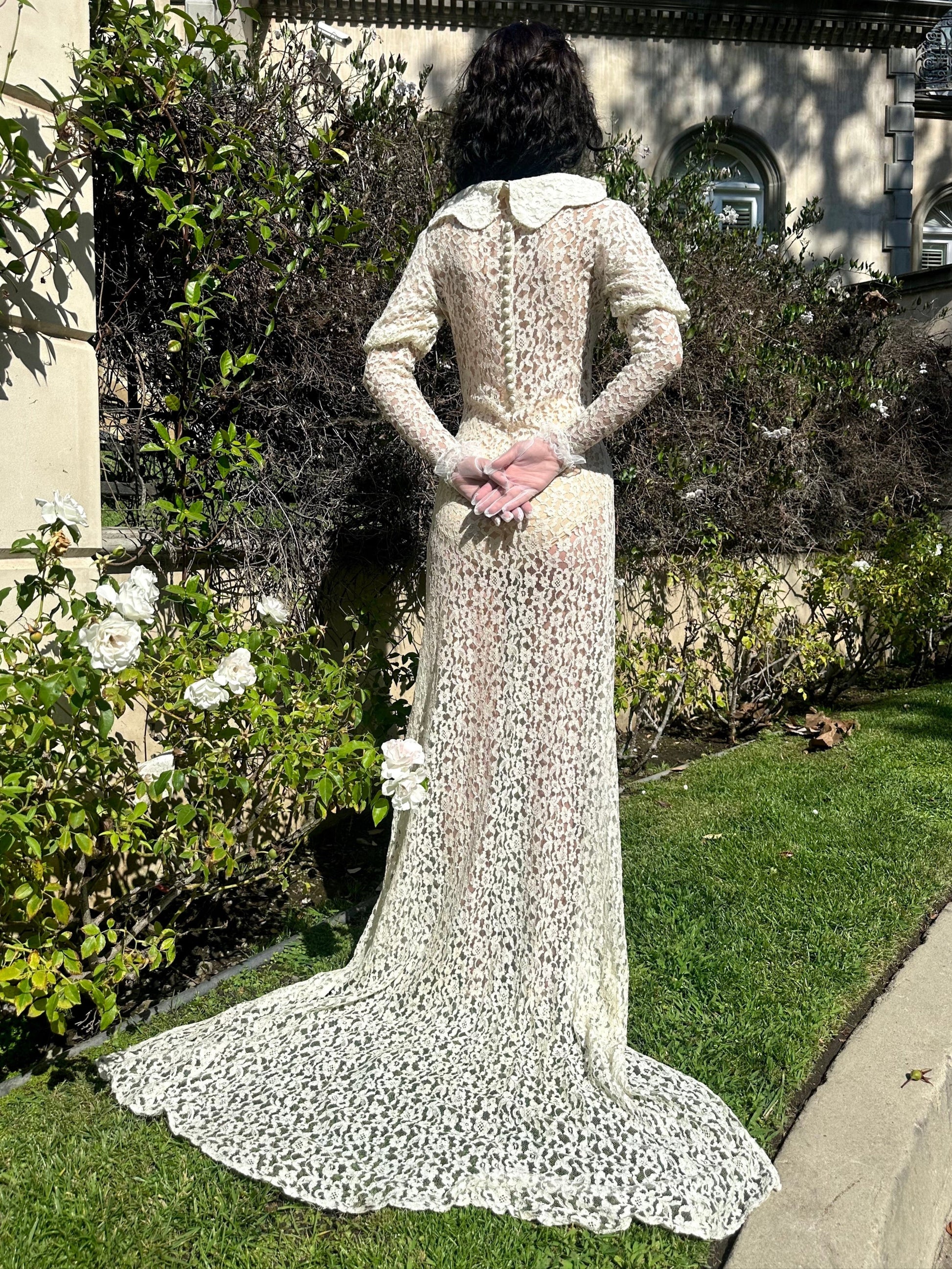 Person wearing a long, white lace dress standing in a garden.