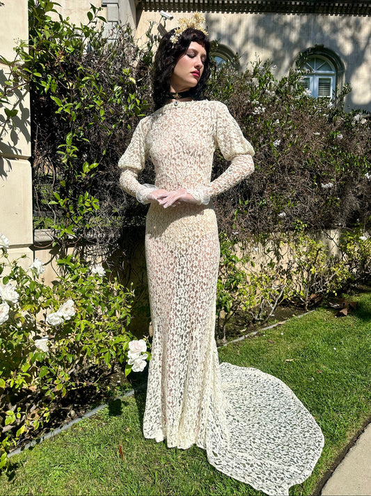 Woman in an antique 1930's white lace wedding dress standing in a garden.